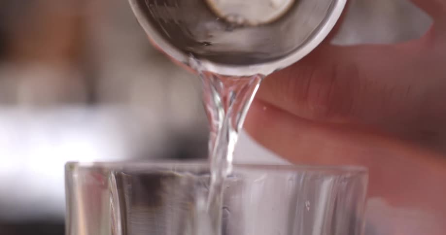 A bartender pours a clear liquid into a jigger before transferring the contents into a drinking glass