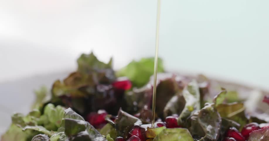 Oil being poured onto a salad with vegetables and fruits on a plate with a white background