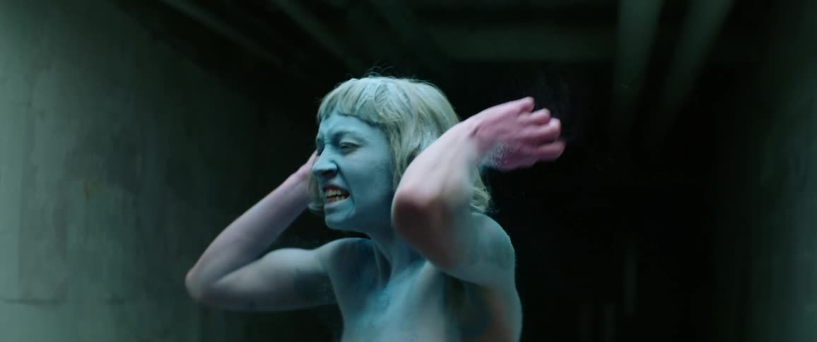 A woman covered in blue and pink powder screaming in a dark hallway