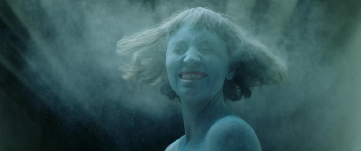 A teenage girl in a tunnel shakes her head and laughs as powder flies off of her