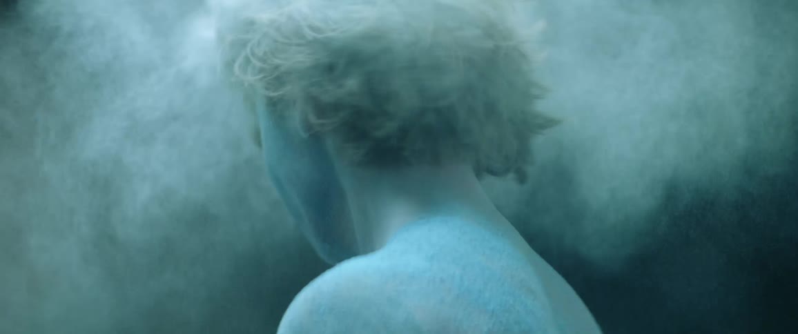 A woman covered in blue powder shaking her head and hair