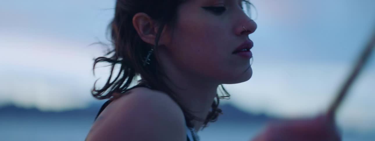Young tattooed woman plays the drums in a desert next to the mountains at sunset
