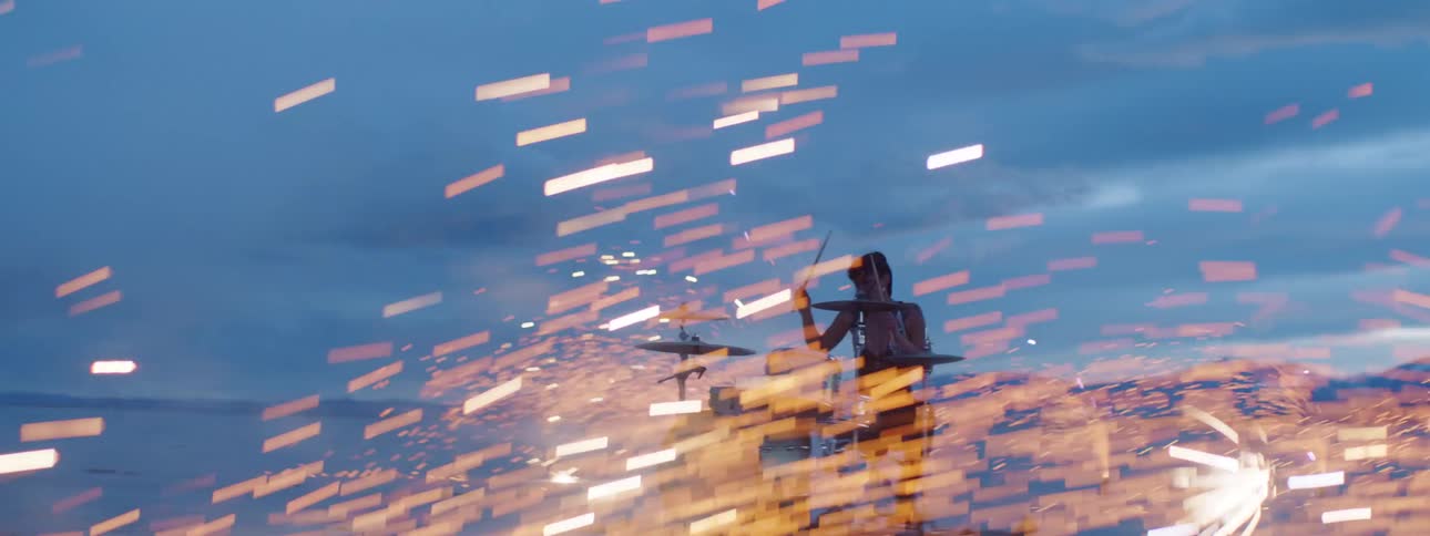 A young woman plays the drums in the desert at sunset as fireworks spend up sparks all around her