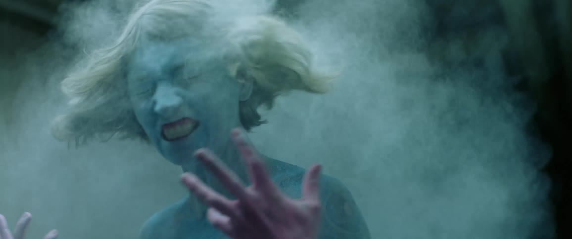 A young woman who is completely coated in blue powder shakes her head rapidly which releases a cloud of powder from her hair