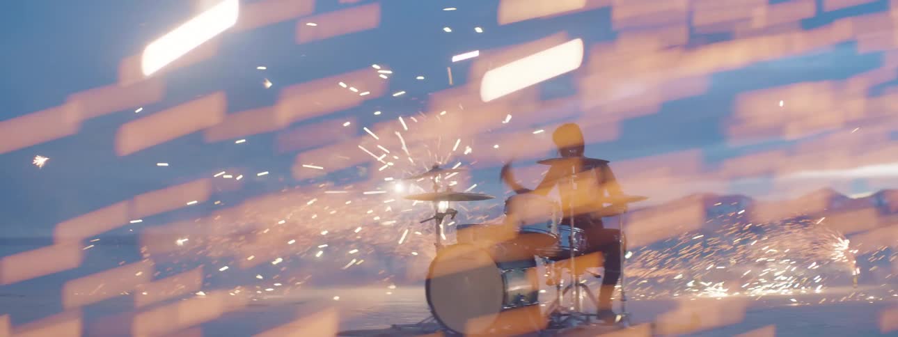 A woman sitting playing drums in the desert surrounded by fireworks