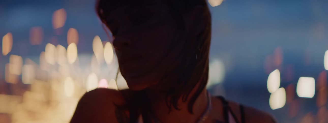 A young woman plays the drums outdoors at night as fireworks send up sparks behind her