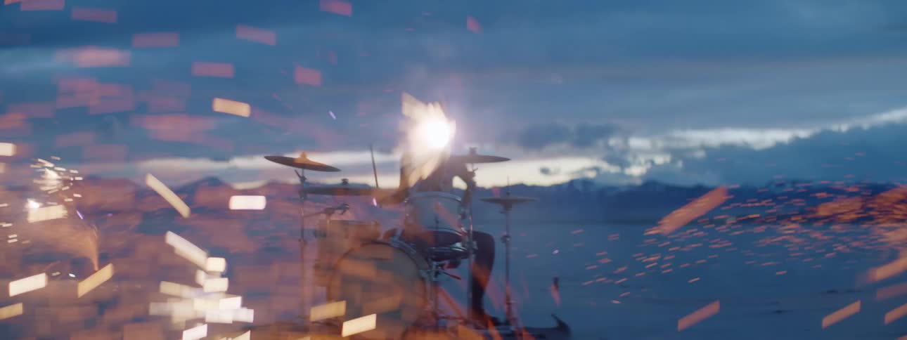 Woman playing drums in desert surrounded by pyrotechnics giving off showers of sparks