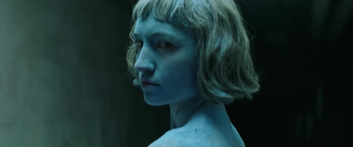 A female painted in blue body paint standing near a wall