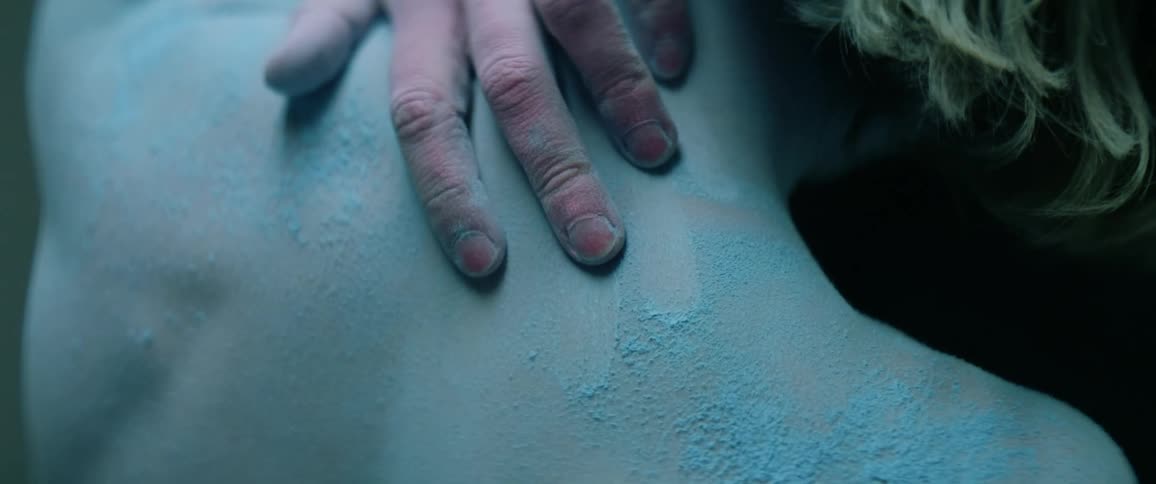 Person wearing blue powder all over body reaches to touch upper back