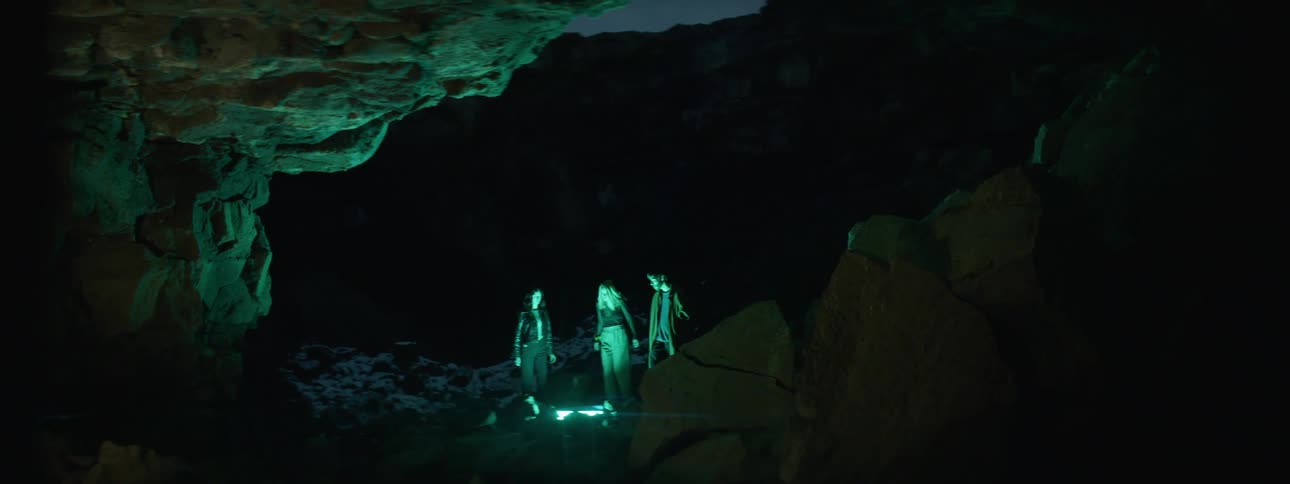A man and two women stand by a fire next to a canyon