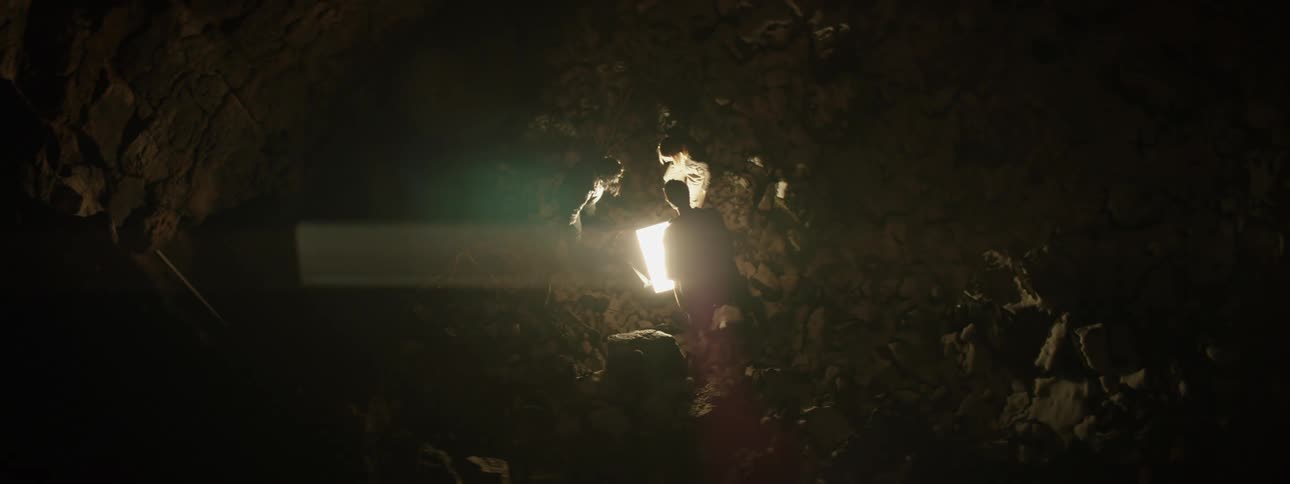 Three teenagers outside at night look down at a bright light