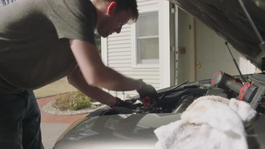 A man walks over to a vehicle and begins working on an engine