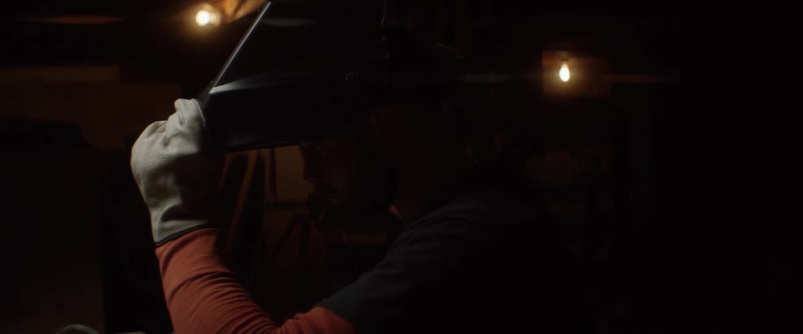 A man puts on a welding mask in a dark area