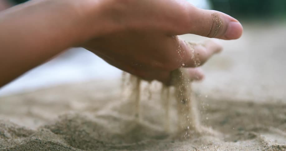 A person lifts a handful of sand and drops it
