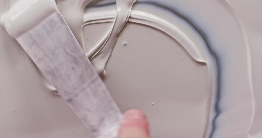 A person is swirling the paint around with a scraper