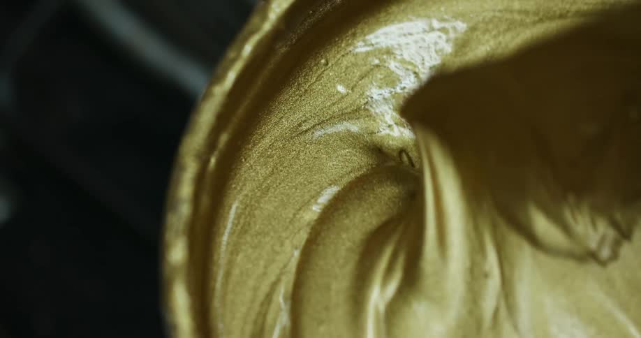 A painter mixes gold painting in a container using a spatula