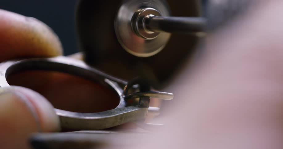 A person uses a polishing machine to polish a ring with its stone removed