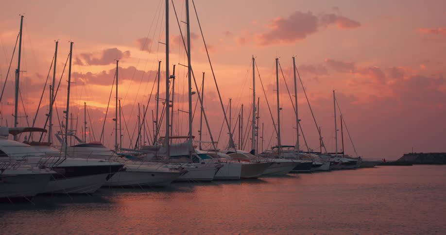 A row of docked sailboats on an ocean at sunset