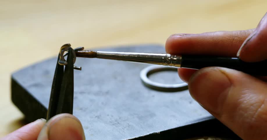 A persons hands using tweezers and a brush to apply glue to a metal