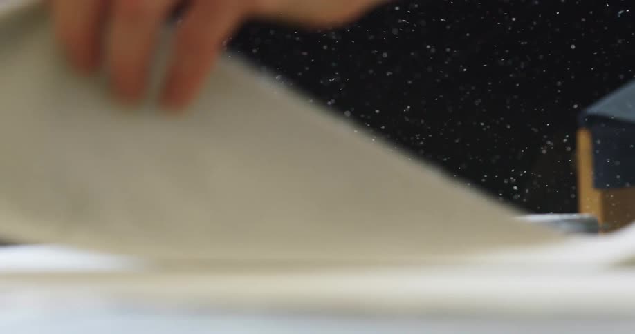 A man folds a piece of paper while dust particles fly around