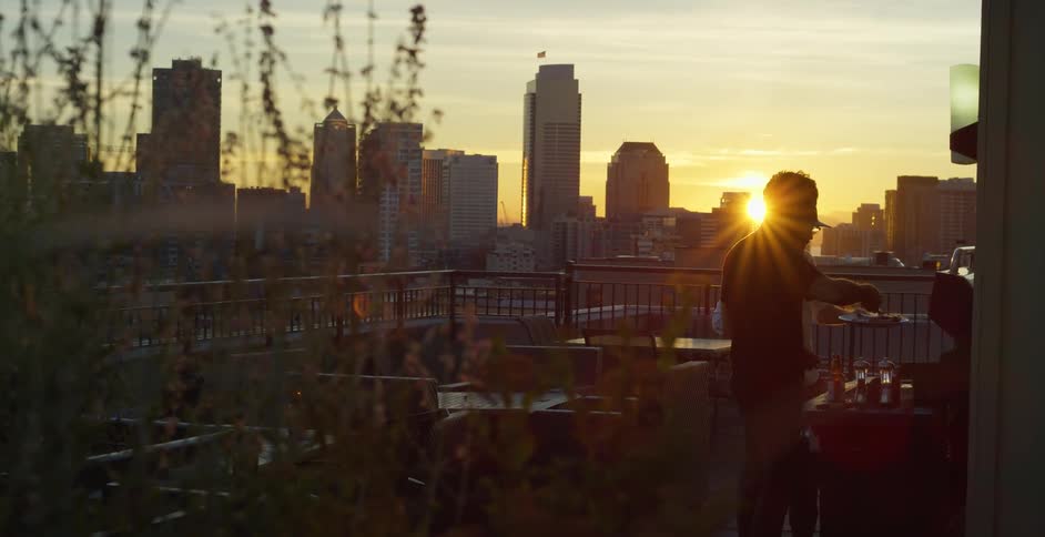 Two men grill outside on a roof top patio in the city