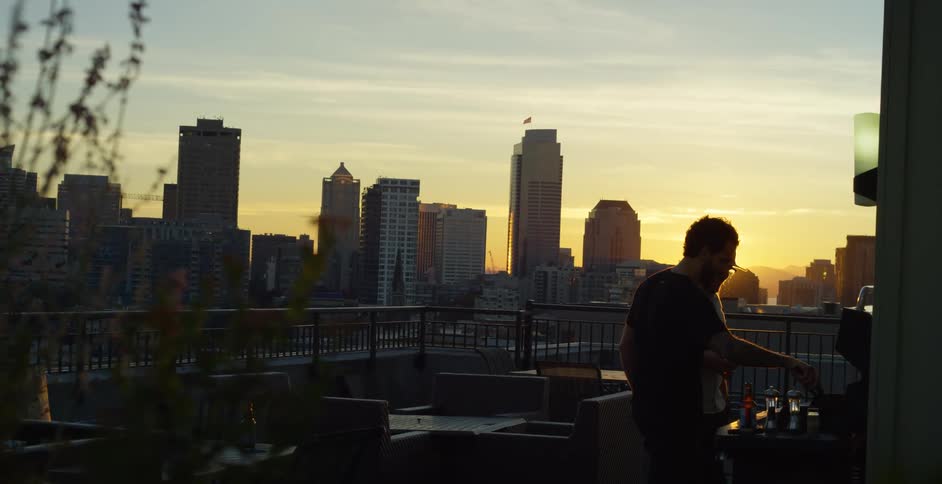 Friends cooking barbecue on a grill in the balcony of a building in the city at sunset