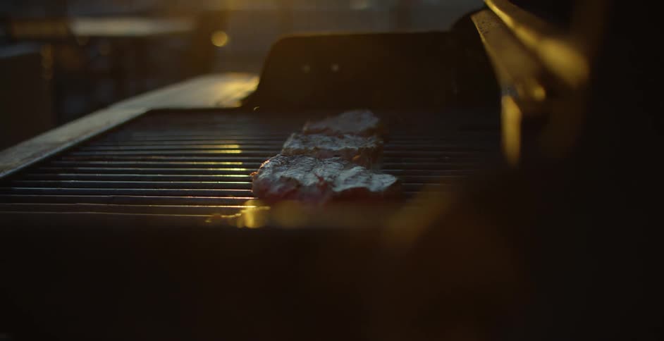 A person is flipping steaks on the grill