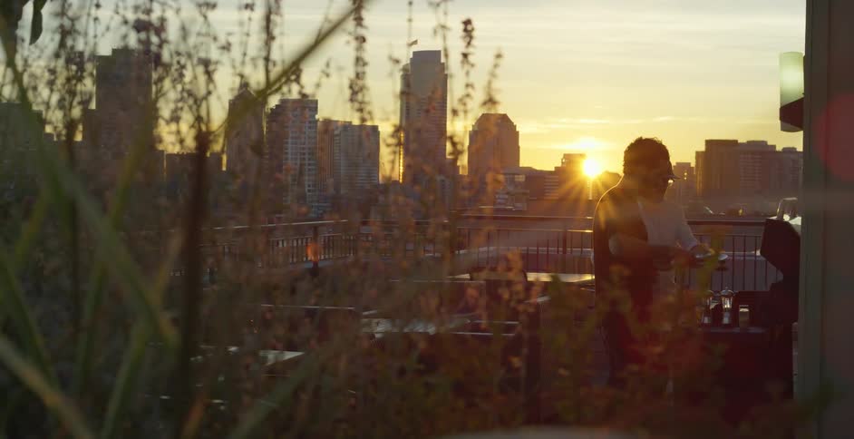 Two men grill outside on their back porch with clear views of a city skyline