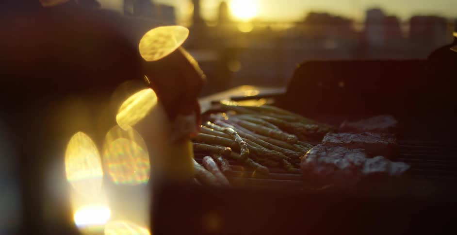 A man at home rubs butter on asparagus on a grill