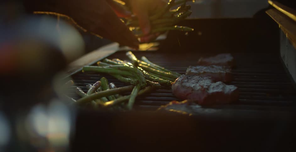 A man places asparagus next to slices of steak on a grill on the rooftop of a building