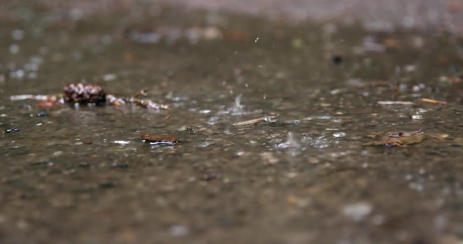 Water splashes up as rainfall hits a puddle on cement