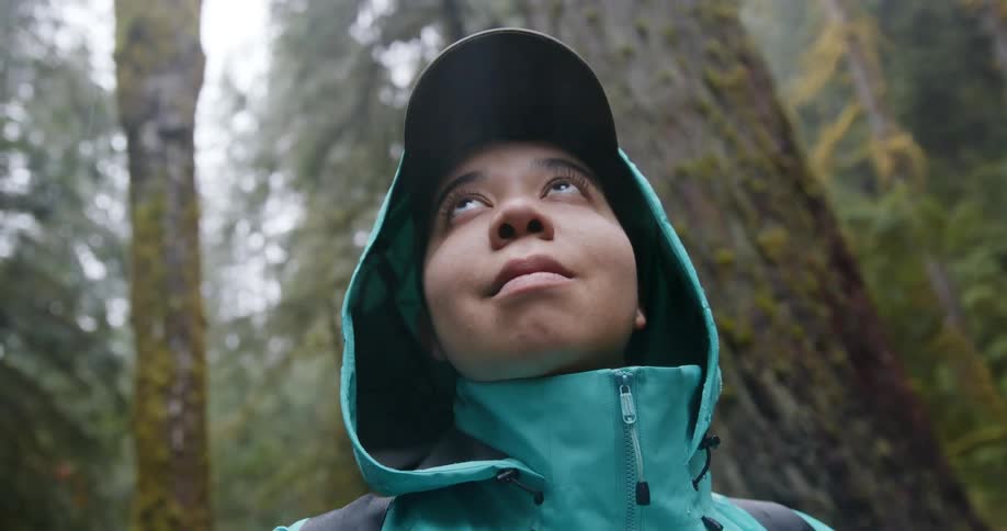 A woman watches the sky as it rains in the forest