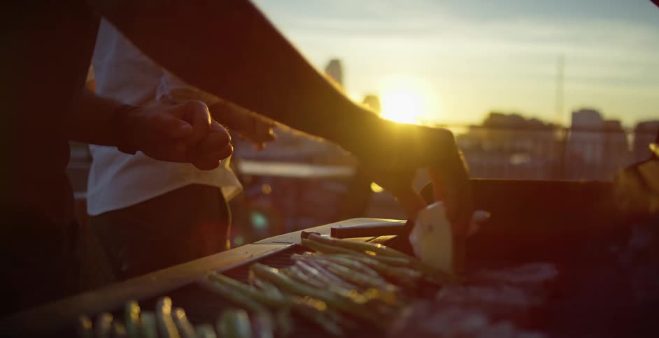 Man cooking a barbecue oils the grill with butter on a balcony in the city at sunset
