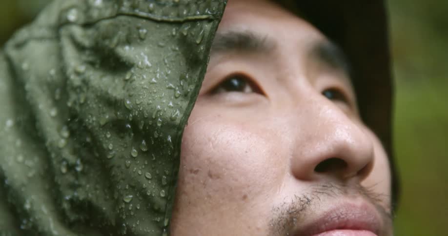 Close up of a mans face wearing a raincoat under the rain in the forest