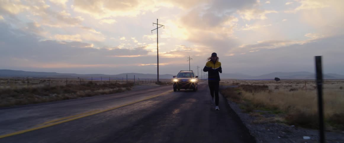 A car is driving on the road while a man is jogging