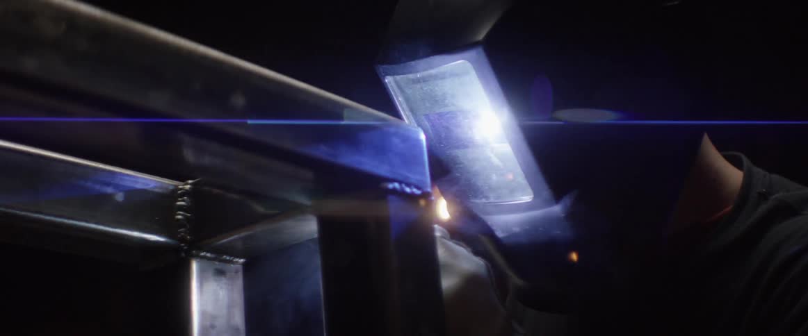 A person wearing a welding mask is welding in a dark area