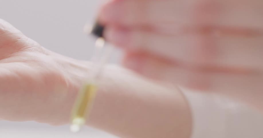 A woman takes a lid off of a bottle and put the liquid from the dropper on her hand