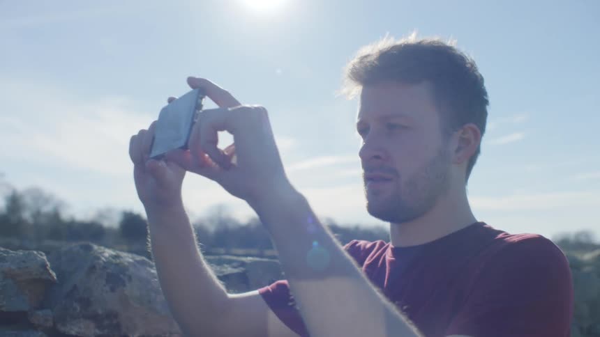 A man snaps a picture with his smartphone outside on a sunny day