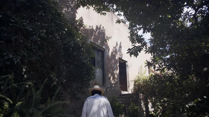 A man wearing a cowboy hat walks towards a stairway leading to the entrance to a building