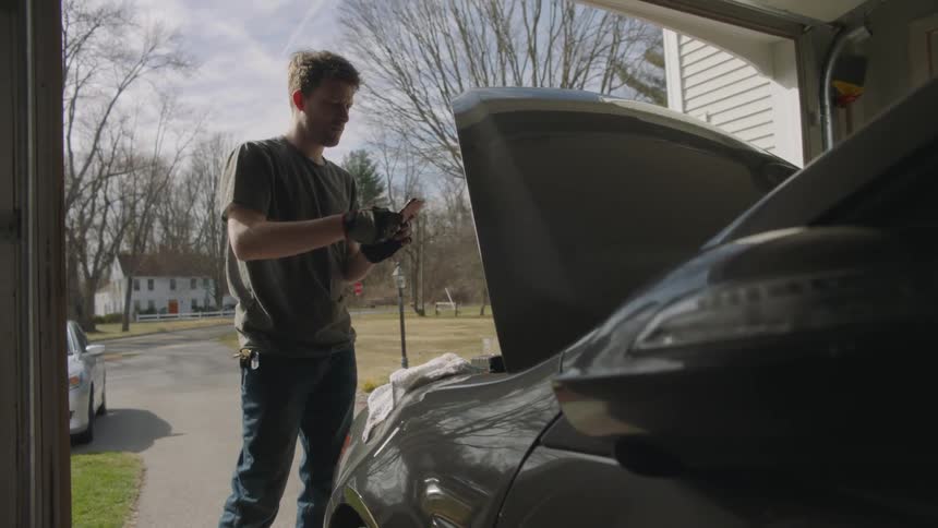 A man takes a photograph of a car with the hood propped up