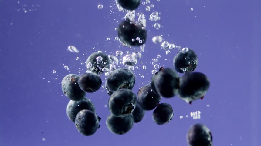 Blueberries create air bubbles while falling into water on a violet background