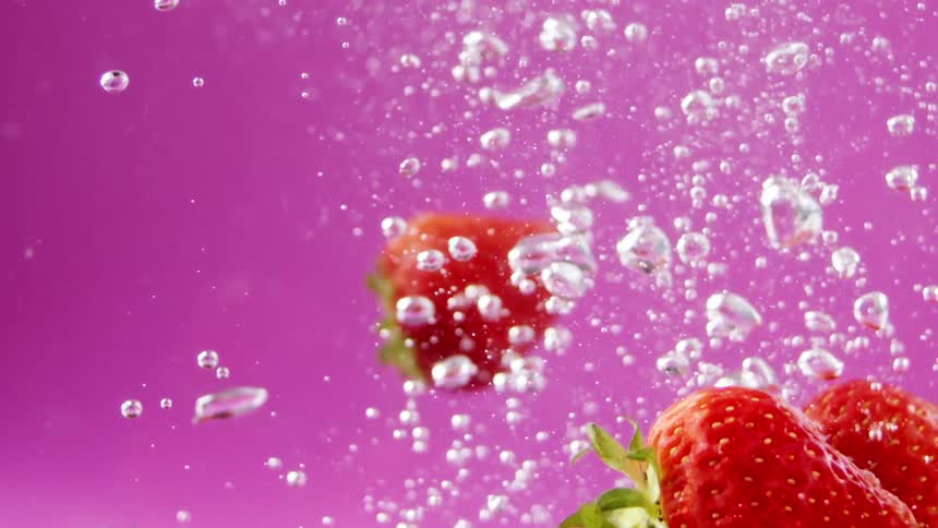 Ripe red strawberries fall into water with a pink background