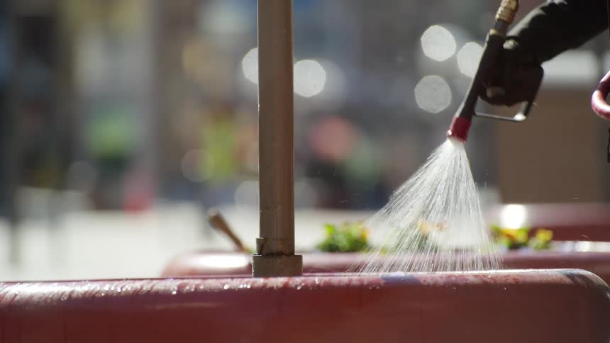 An employee watering flowers outside in a city