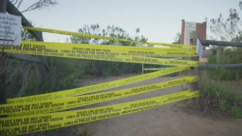 Police tape bars the entrance to an area surrounded by a wooden fence