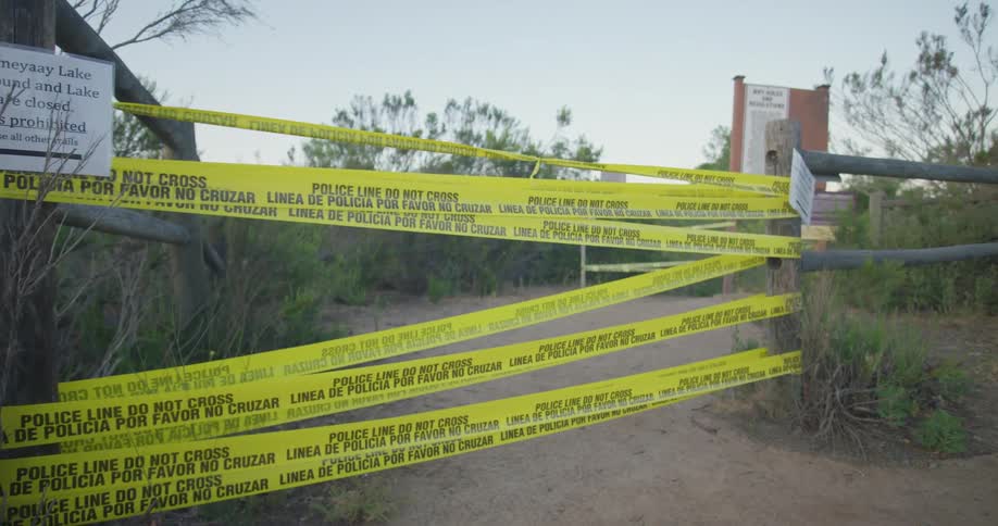 Police tape bars the entrance to an area surrounded by a wooden fence