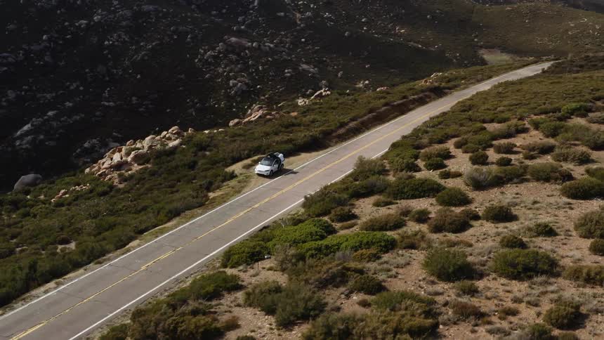 White vehicle is parked alongside a highway near the mountains