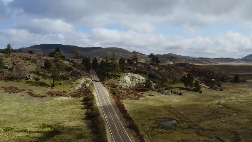 An aerial view of a single electric car driving down a road in the country
