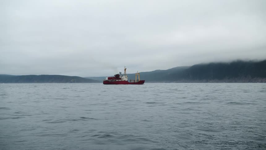 A ship floats in the ocean in front of mountains on a cloudy day.