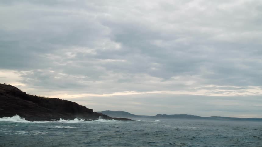 Waves crash into rocks on the ocean at sunset.