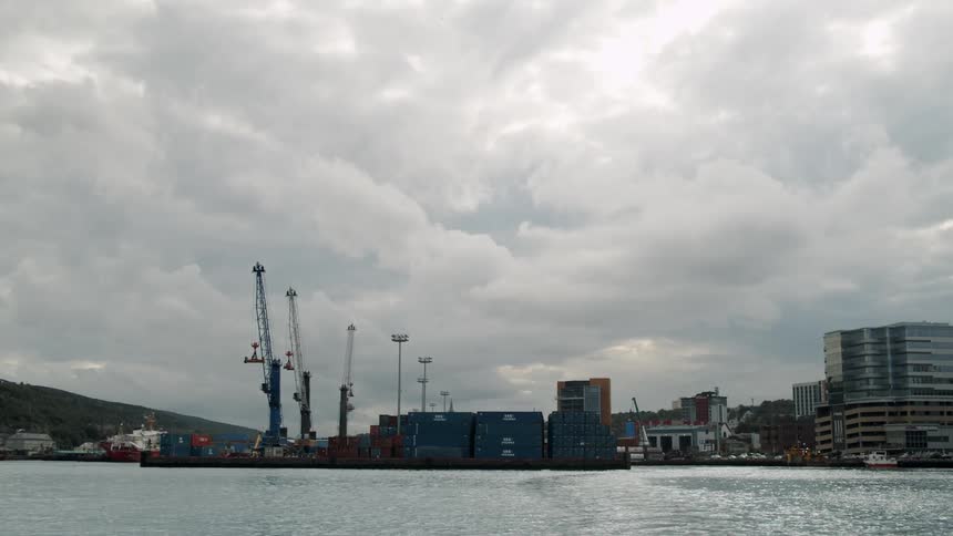 A shipping yard on the coast of a city under a cloudy sky